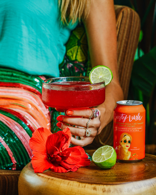 Busty Lush She's Marvelous alcohol-free mezcalita in a coupe glass with lime, held beside the orange can