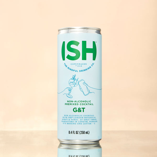 Single can of ISH Gin & Tonic on a mirrored tabletop with a soft peach background, reflecting the alcohol-free cocktail’s elegant, modern design.