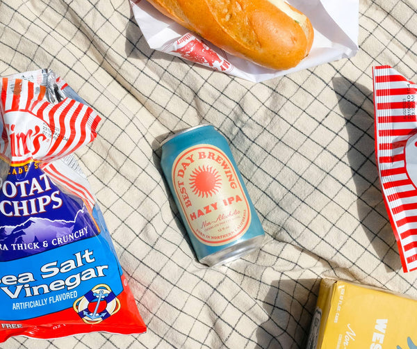 Best Day Hazy IPA non-alcoholic beer can on a picnic blanket with chips and a baguette