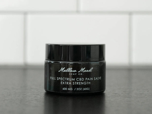 Black jar of Mellow Mood Hemp Co. Full Spectrum CBD Pain Salve, Extra Strength, 600 mg / 2 oz, on a dark countertop.