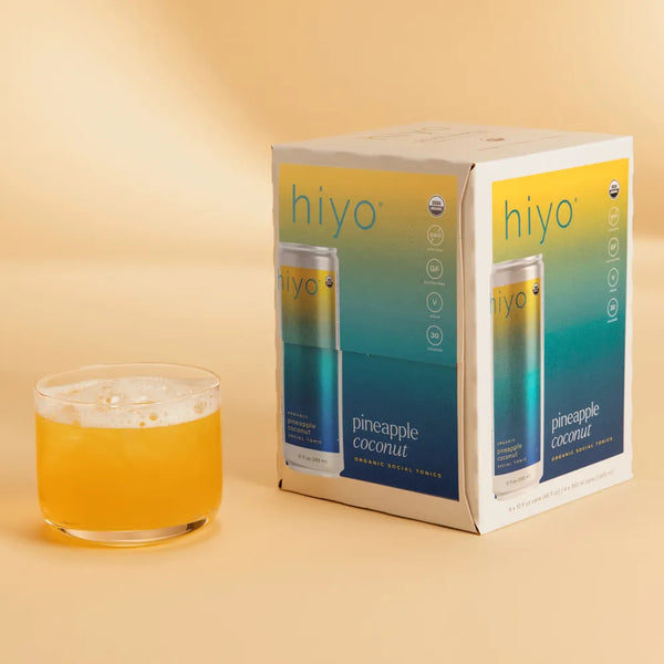 hiyo Pineapple Coconut alcohol-free social tonic four-pack box beside a poured glass