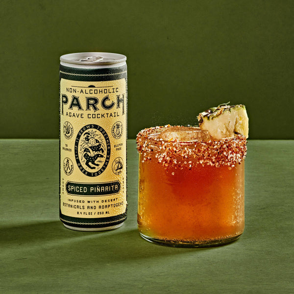 PARCH Spiced Pinarita alcohol-free agave cocktail can beside a chili-rimmed glass with pineapple garnish