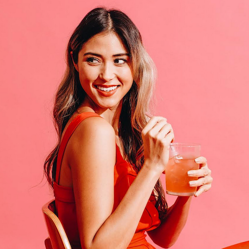 Woman in red dress holding a glass of Heywell cherry limeade alcohol-free functional beverage