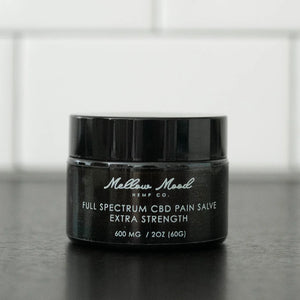 Black jar of Mellow Mood Hemp Co. Full Spectrum CBD Pain Salve, Extra Strength, 600 mg / 2 oz, on a dark countertop.
