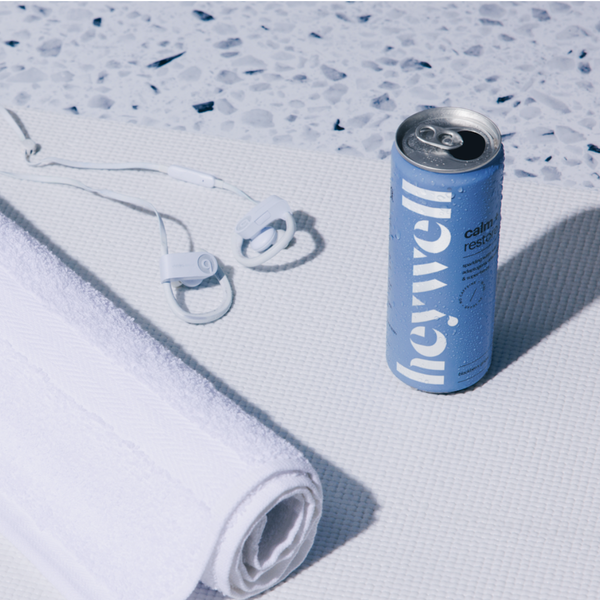Heywell Calm + Restore alcohol-free sparkling water can on a yoga mat with earbuds and towel