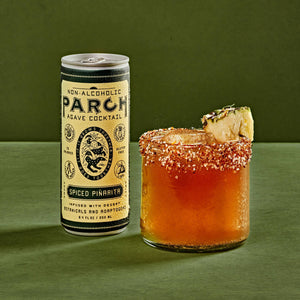 PARCH Spiced Pinarita alcohol-free agave cocktail can beside a chili-rimmed glass with pineapple garnish