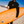 Surfer in wetsuit holding a hiyo Peach Mango alcohol-free functional seltzer can with orange surfboard on beach